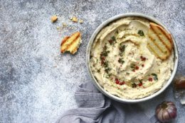 White bean hummus with baked garlic and dried herbs in a bowl over grey slate, stone or concrete background.Top view with copy space.