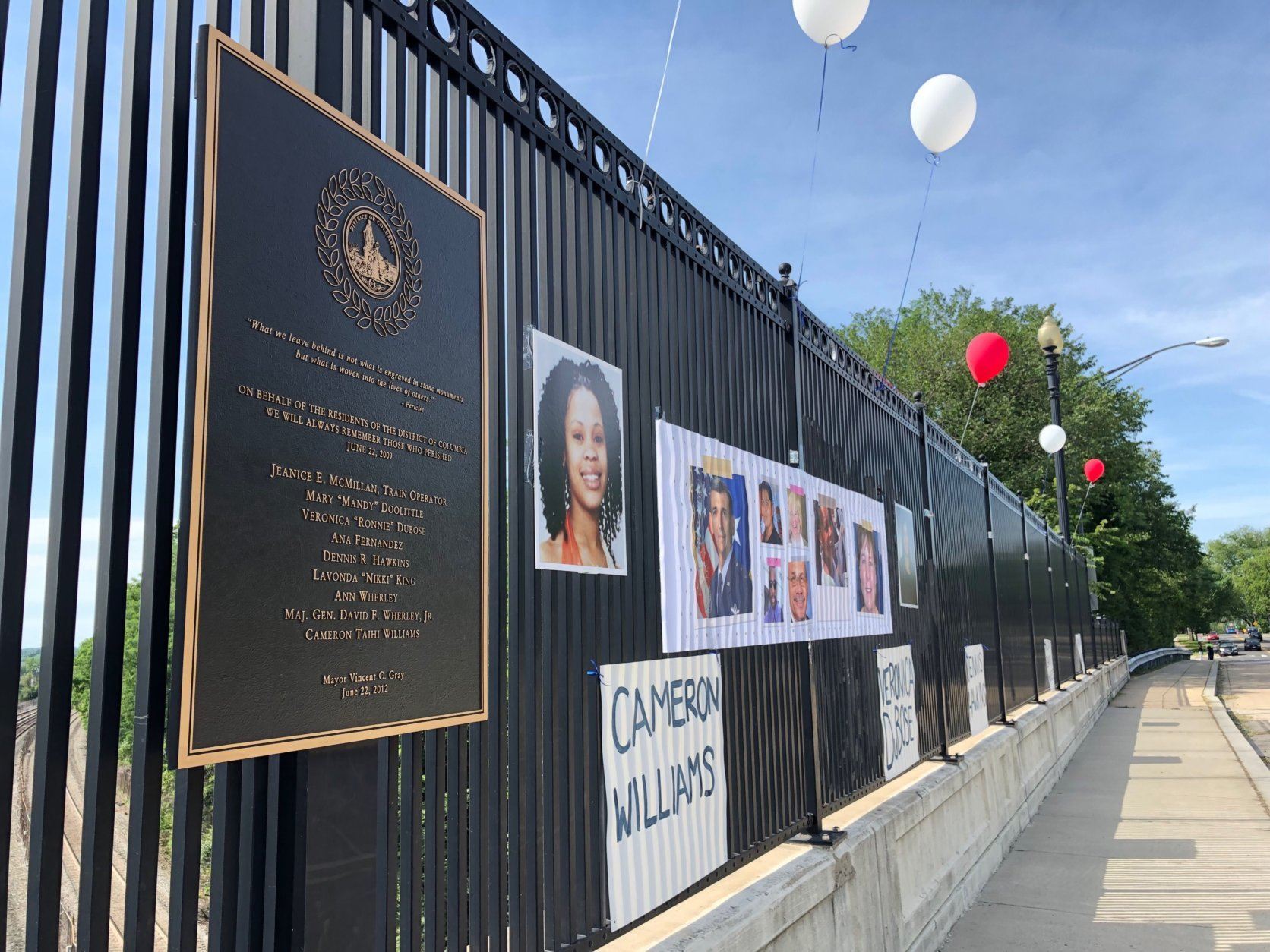 On the New Hampshire Avenue bridge over the tracks where the 2009 Metro crash happened, the names of those killed were posted along with photos. Red and white balloons were tied to the fence. (WTOP/Kate Ryan) 