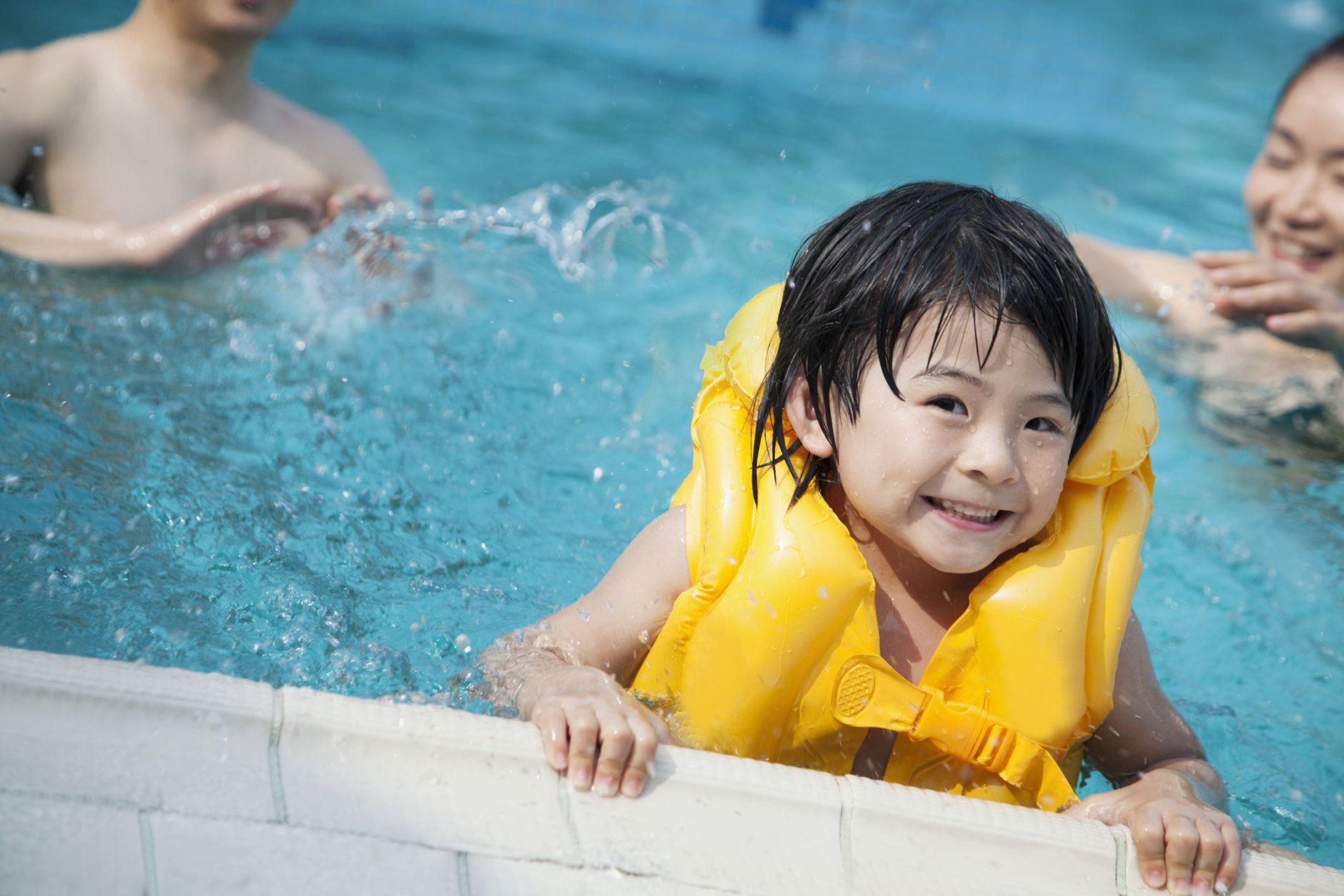 Portrait of smiling son in the water and holding onto the pools edge with family in the background