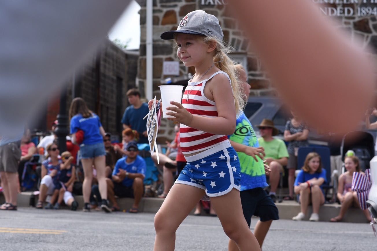 A little girl dashes back to her seat after getting a fan being given out by one of the units at the Takoma Park Fourth of July parade. (WTOP/Kate Ryan)