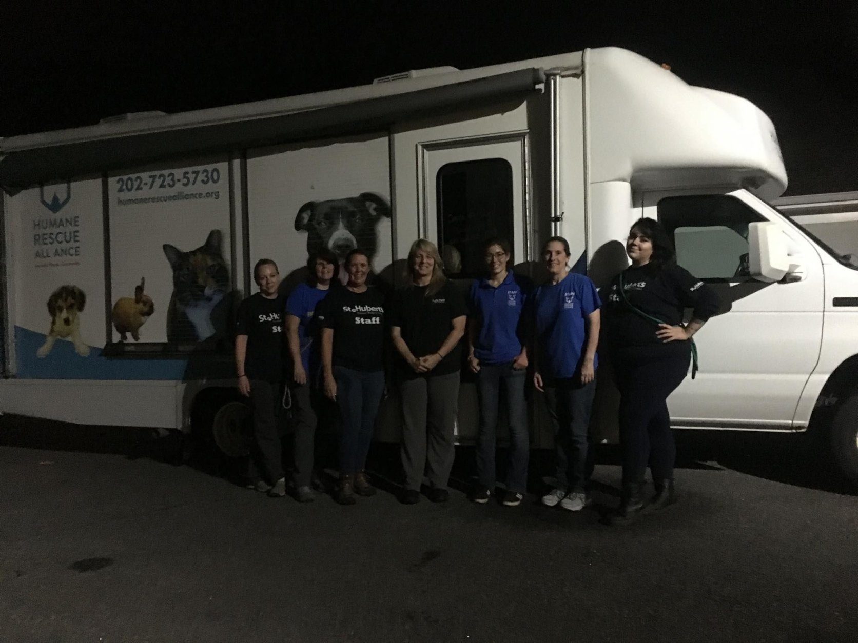 Humane Rescue Alliance personnel pose for a photo in front of a van. Night has fallen.
