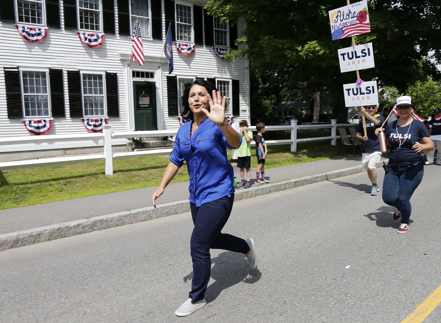 Democratic presidential candidate U.S. Rep. Tulsi Gabbard, D-Hawaii, waves along the parade route as she runs to catch up to her supporters during the Fourth of July Parade, Thursday, July 4, 2019, in Amherst. (AP Photo/Mary Schwalm)