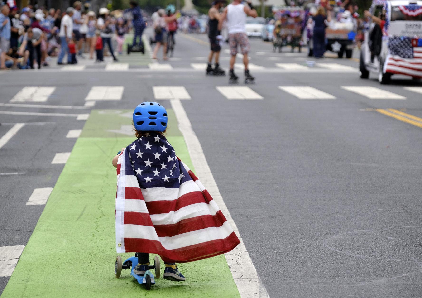 Two and a half year old Zacky Kaplan rides his scooter while draped in the American flag as he makes his way along the parade route during the Santa Monica Fourth of July Parade on Thursday, July 4, 2019 in Santa Monica, Calif. (AP Photo/Richard Vogel)