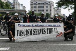 Antifa protesters pose with a sign in front of Washington, D.C. police officers, as members of the far-right rally against conservative censorship in social media. Trump supporters and anti-fascist organizers held dueling rallies across the street from each other, leading to high tensions as D.C. and U.S. Park Police largely held the peace. (WTOP/Alejandro Alvarez)