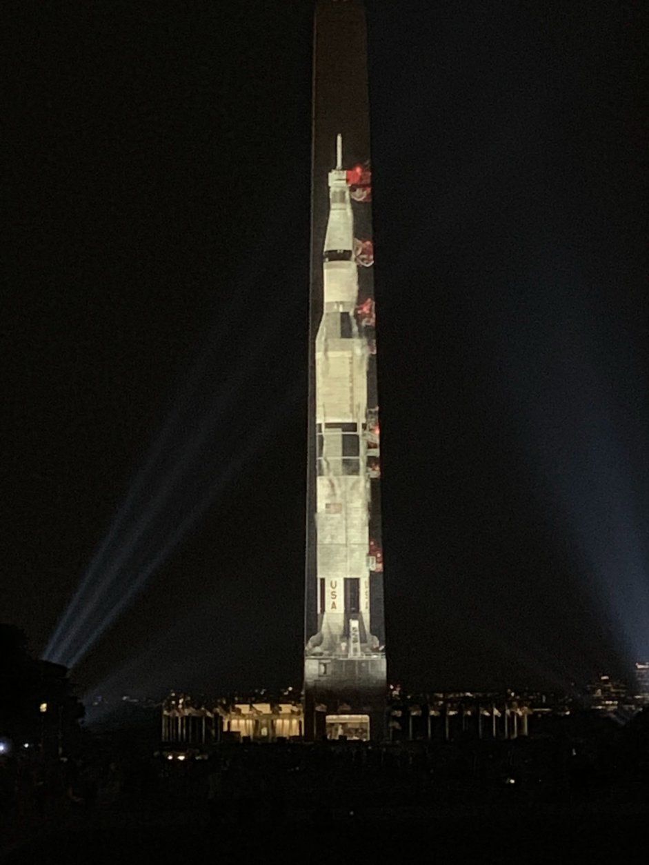 A projection of a 363-foot Saturn V rocket projected on the Washington Monument
