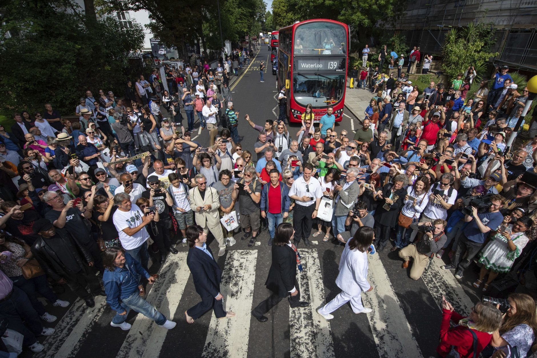 Thousands of fans gather to walk across the Abbey Road zebra crossing, on the 50th anniversary of British pop musicians The Beatles doing it for the cover of their album 'Abbey Road' in St Johns Wood in London, Thursday, Aug. 8, 2019. They aimed to cross 50 years to the minute since the 'Fab Four' were photographed for the album.(Dominic Lipinski/PA via AP)