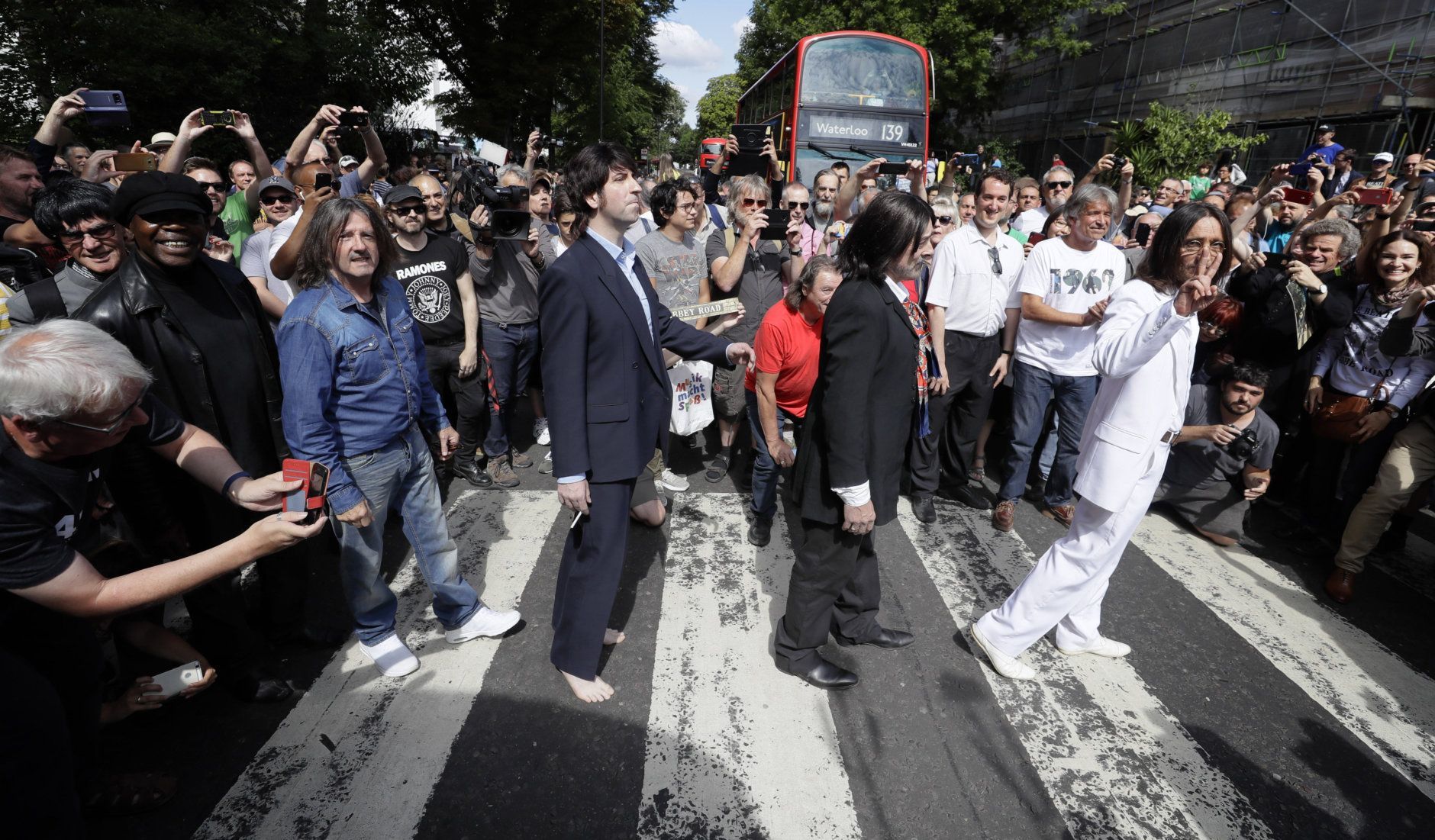 Fans dressed as lookalikes walk across the Abbey Road zebra crossing on the 50th anniversary of British pop musicians The Beatles doing it for their album cover of 'Abbey Road' in St Johns Wood in London, Thursday, Aug. 8, 2019. They aimed to cross 50 years to the minute since the 'Fab Four' were photographed for the album. (AP Photo/Kirsty Wigglesworth)