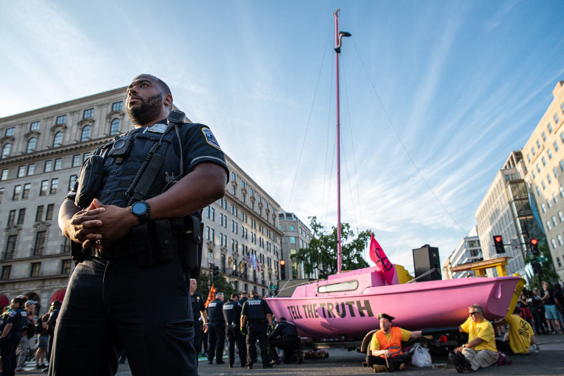 While D.C. police pushed onlookers back from the sailboat as they worked to extract bound protesters, about 100 people remained to cheer on their colleagues as police wheeled in a generator and electric saw. (WTOP/Alejandro Alvarez)