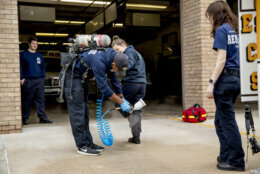 Volunteer EMT Ronald Felix, a full time police officer for Montgomery County, Md., second from left, sanitizes the shoes of his fellow volunteer EMT workers Alexandra Sachs, center, and Katherine Weber, right, after he finishes spraying an ambulance before they go out on calls at Bethesda-Chevy Chase Rescue Squad, Saturday, April 4, 2020, in Bethesda, a suburb of Washington. (AP Photo/Andrew Harnik)