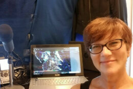 Female journalist smiling next to a laptop computer and microphone.