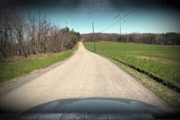 a dirt road is seen ahead from the perspective of a driver looking thru windshield