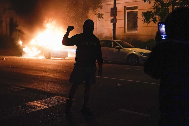 <p>A demonstrator is filmed in front of a burning car during a protest of the death of George Floyd, Sunday, May 31, 2020, near the White House in Washington. Floyd died after being restrained by Minneapolis police officers. (AP Photo/Evan Vucci)</p>
