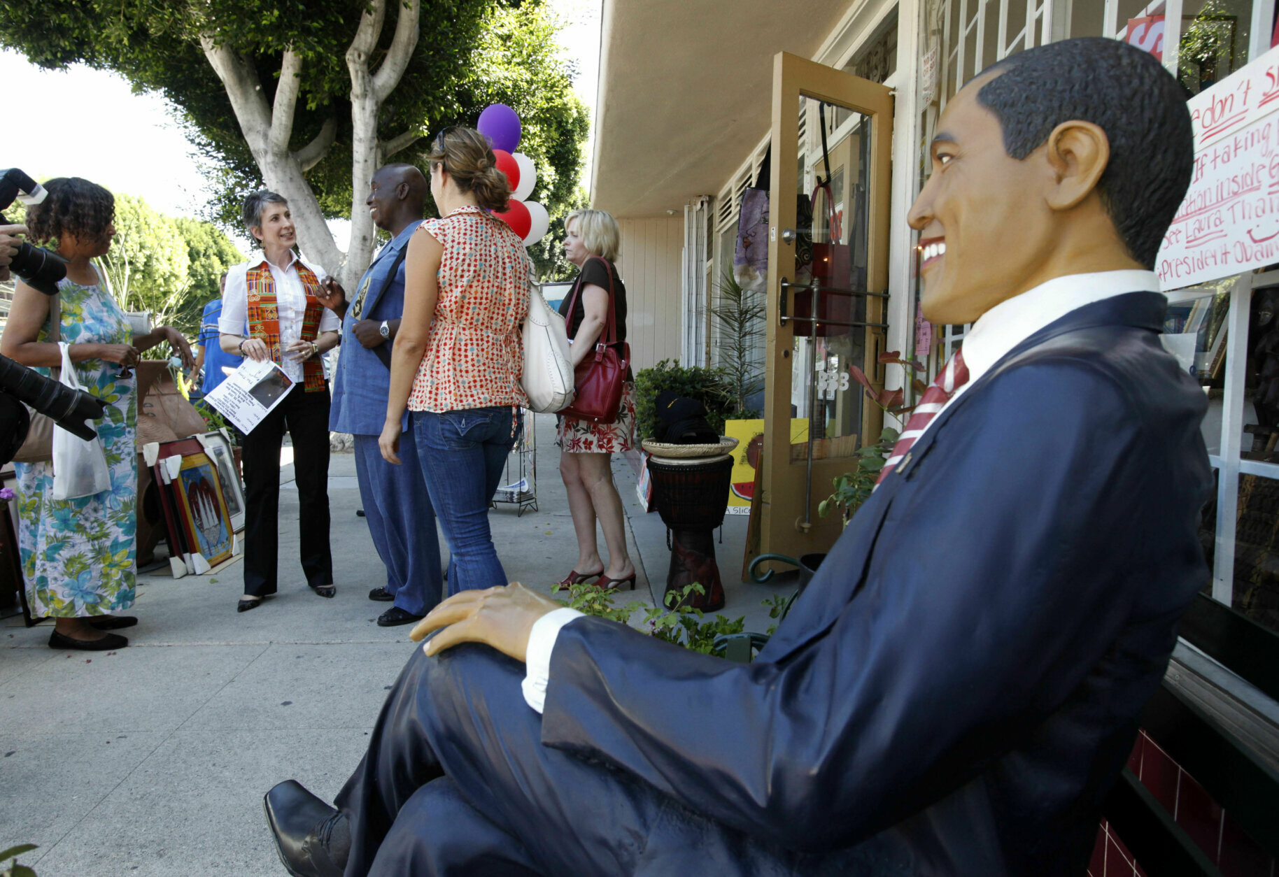 A figure of President Barack Obama on a park bench is in the foreground as Carly Fiorina, Republican nominee for the U.S. Senate from California, second from left, talks with people taduring a visit to a Juneteenth celebration at Leimert Park in the Crenshaw District of Los Angeles Saturday, June 19, 2010.  (AP Photo/Reed Saxon)
