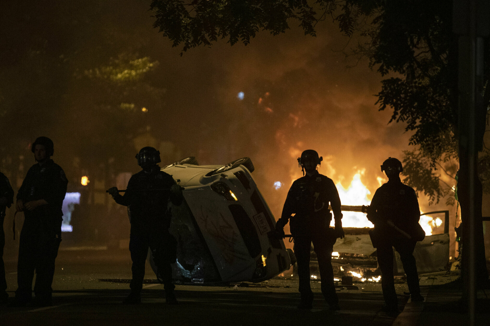 <p>Police stand near an overturned vehicle and a fire as demonstrators protest the death of George Floyd, Sunday, May 31, 2020, near the White House in Washington. Floyd died after being restrained by Minneapolis police officers (AP Photo/Alex Brandon)</p>
