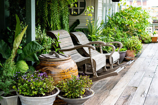 Wooden rocking chairs in a cottage garden porch setting on wooden floor in vintage Thai botanical garden, with traditional Thai old water jar decoration.