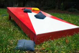 Close-up of red and white cornhole board on green grass with blue and yellow beanbags.