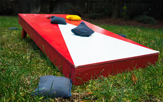 Close-up of red and white cornhole board on green grass with blue and yellow beanbags.