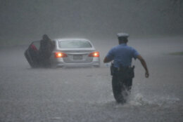 A Philadelphia police officer rushes to help a stranded motorist during Tropical Storm Isaias, Tuesday, Aug. 4, 2020, in Philadelphia. The storm spawned tornadoes and dumped rain during an inland march up the U.S. East Coast after making landfall as a hurricane along the North Carolina coast. (AP Photo/Matt Slocum)