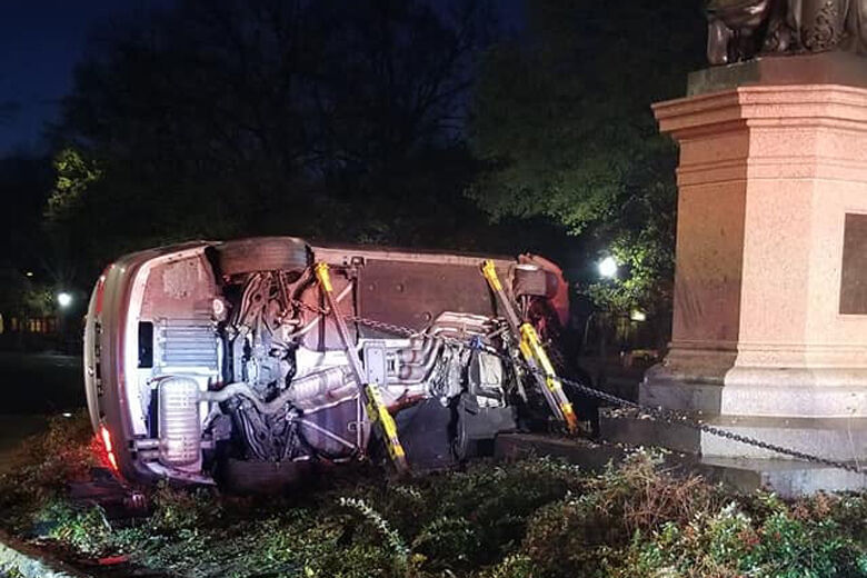 Overturned car resting against statue.