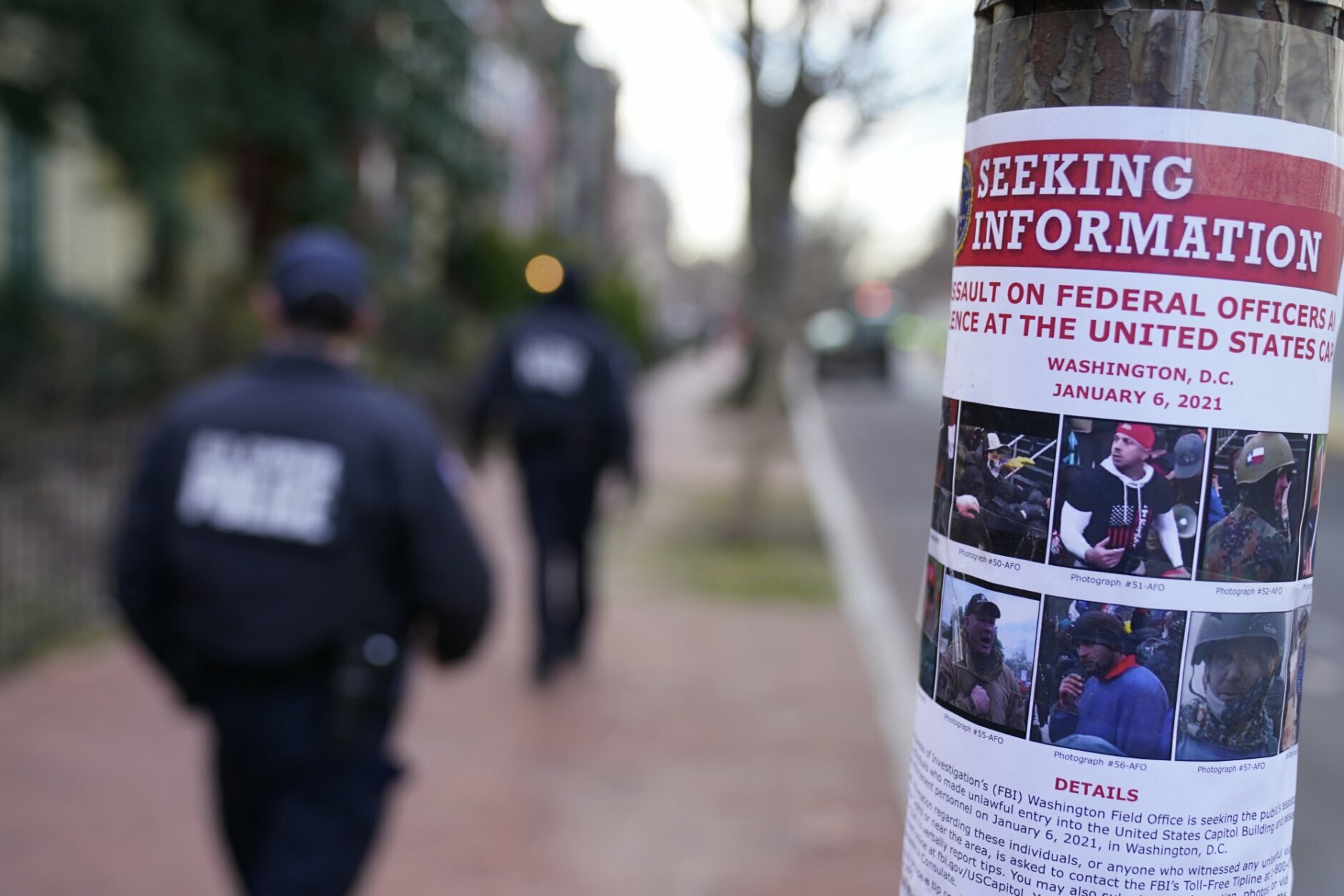 Capitol police walk past a poster seeking information on individuals who attacked the Capitol building, Tuesday, Jan. 19, 2021, in Washington. Security n been heightened ahead of President-elect Joe Biden's inauguration ceremony. (AP Photo/David Goldman)