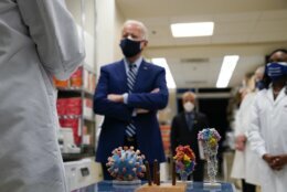 With a model of the Covid-19 virus displayed, President Joe Biden listens as Dr. Barney Graham, left, speaks during a visit at the Viral Pathogenesis Laboratory at the National Institutes of Health (NIH), Thursday, Feb. 11, 2021, in Bethesda, Md. Kizzmekia Corbett, an immunologist with the Vaccine Research Center at the NIH listens at right. (AP Photo/Evan Vucci)