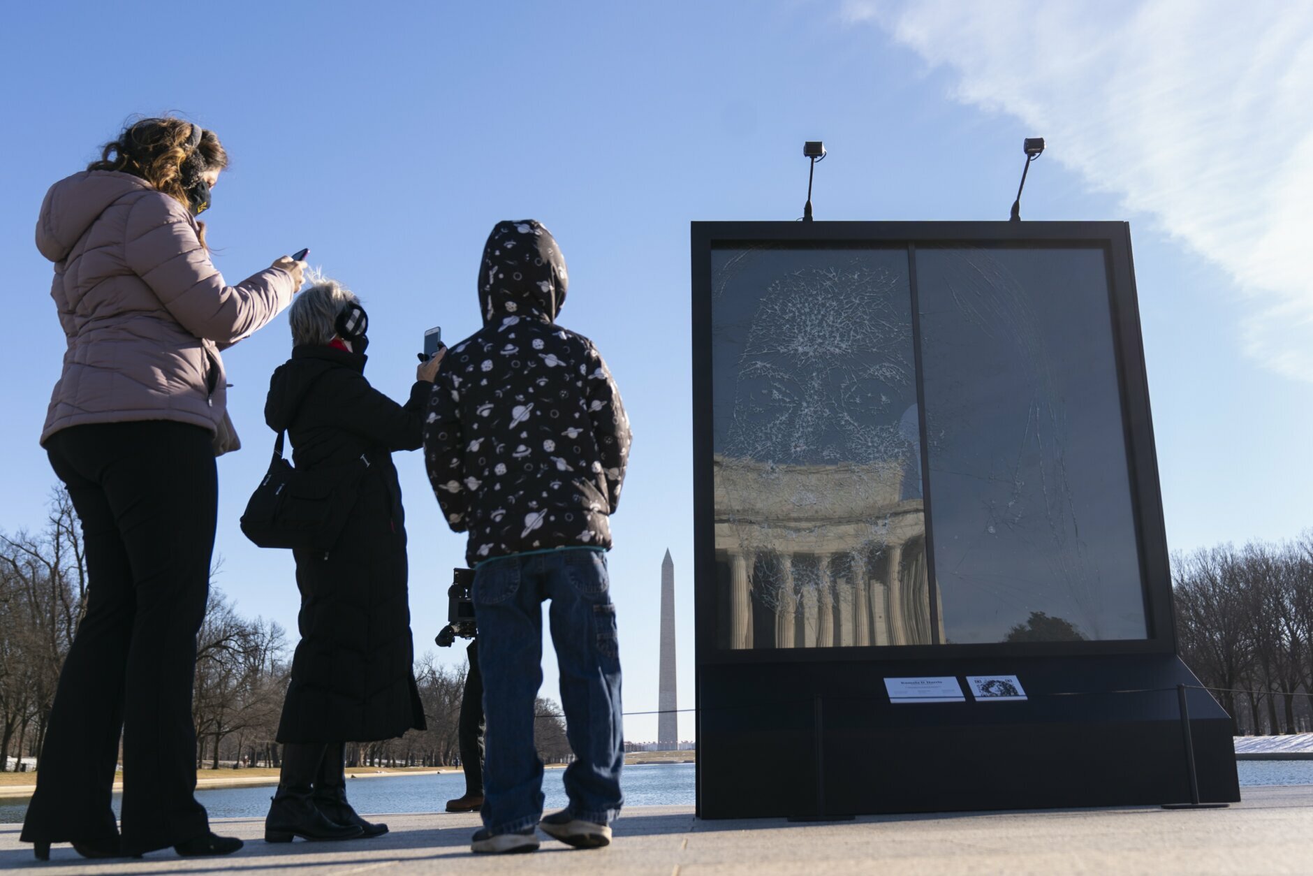 People photograph the installation "Vice President Kamala Harris Glass Ceiling Breaker" at the Lincoln Memorial in Washington, Wednesday, Feb. 4, 2021. Vice President Kamala Harris' barrier-breaking career has been memorialized in a portrait depicting her face emerging from the cracks in a massive sheet of glass. Using a photo of Harris that taken by photographer Celeste Sloman, artist Simon Berger lightly hammered on the slab of laminated glass to create the portrait of Harris. The Washington Monument is seen in the distance and the Lincoln Memorial is reflected. (AP Photo/Carolyn Kaster)