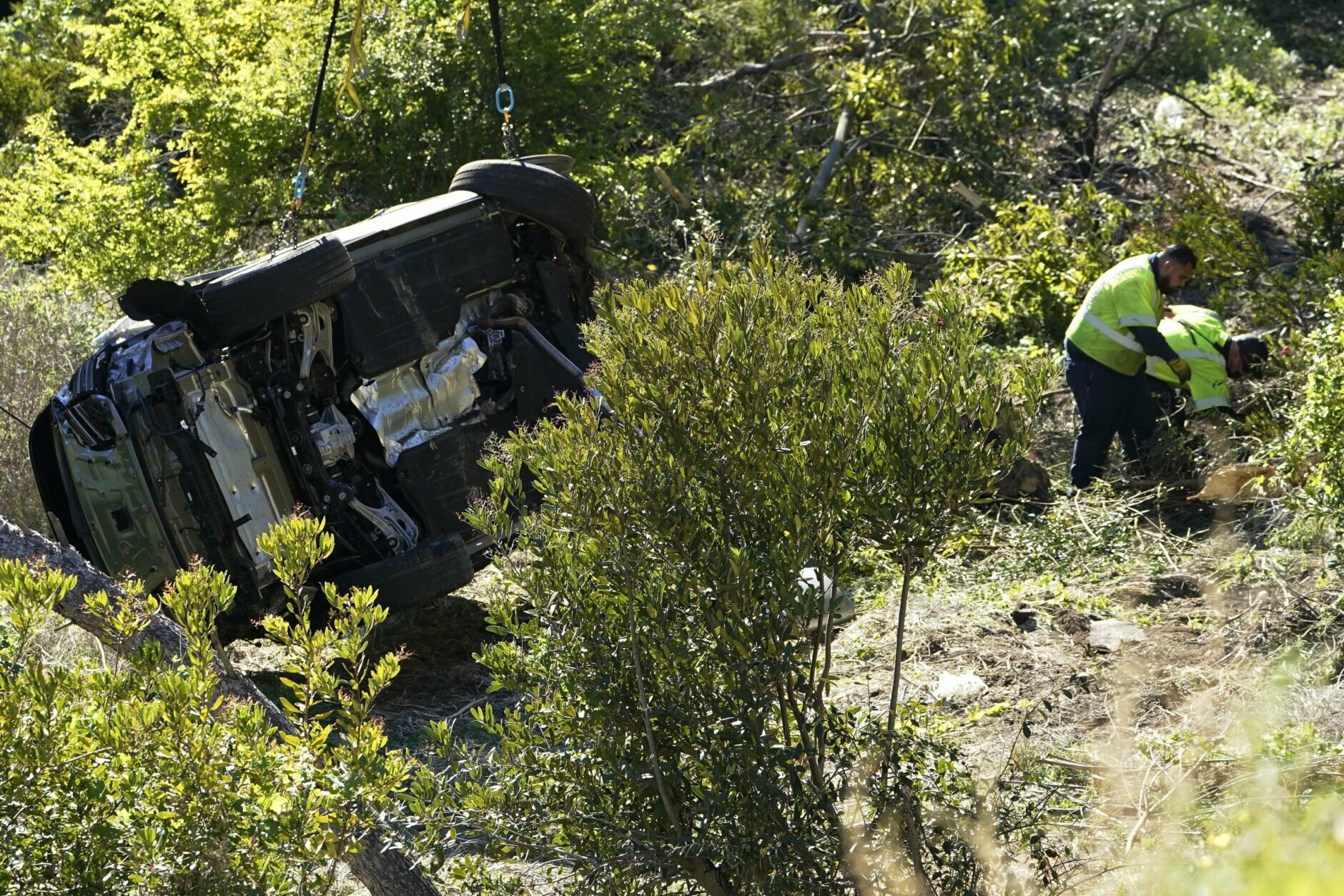 Workers remove debris near a vehicle on its side after a rollover accident involving golfer Tiger Woods Tuesday, Feb. 23, 2021, in Rancho Palos Verdes, Calif., a suburb of Los Angeles. Woods suffered leg injuries in the one-car accident and was undergoing surgery, authorities and his manager said. (AP Photo/Marcio Jose Sanchez)