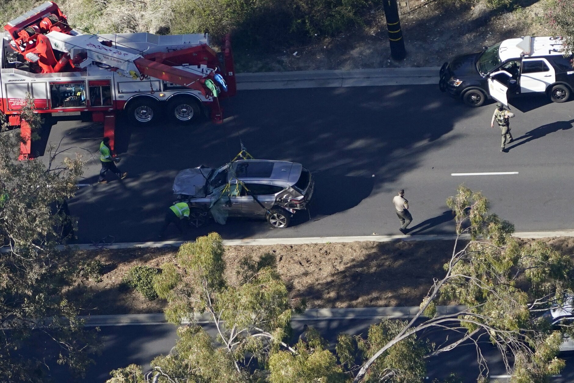 Workers move a vehicle after a rollover accident involving golfer Tiger Woods Tuesday, Feb. 23, 2021, in Rancho Palos Verdes, Calif. a suburb of Los Angeles. Woods suffered leg injuries in the one-car accident and was undergoing surgery, authorities and his manager said. (AP Photo/Mark J. Terrill)