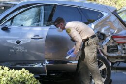 A law enforcement officer looks over a damaged vehicle following a rollover accident involving golfer Tiger Woods, Tuesday, Feb. 23, 2021, in the Rancho Palos Verdes suburb of Los Angeles. Woods suffered leg injuries in the one-car accident and was undergoing surgery, authorities and his manager said. (AP Photo/Ringo H.W. Chiu)