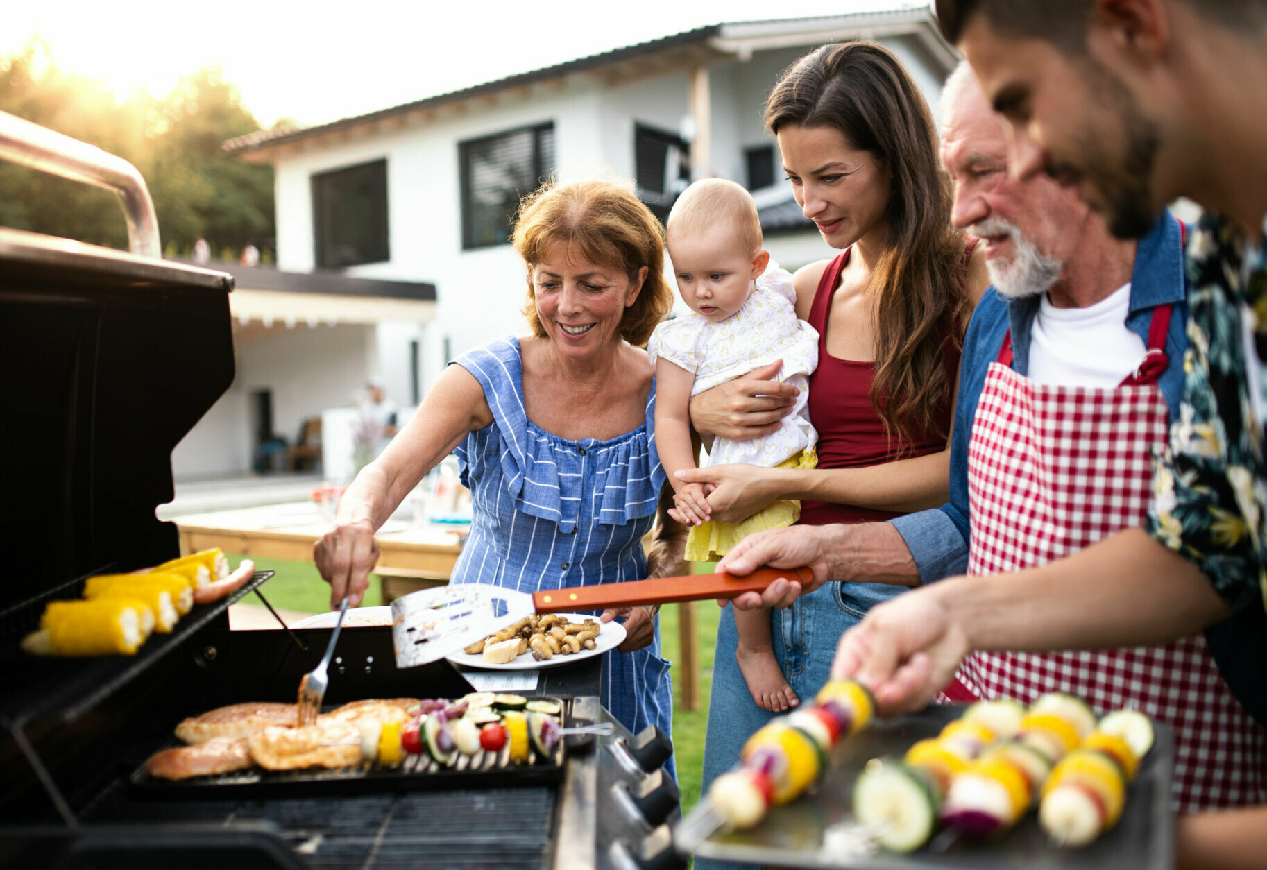 Portrait of multigeneration family outdoors on garden barbecue, grilling and talking.
