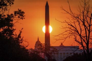 The sun rises behind the Washington Monument.