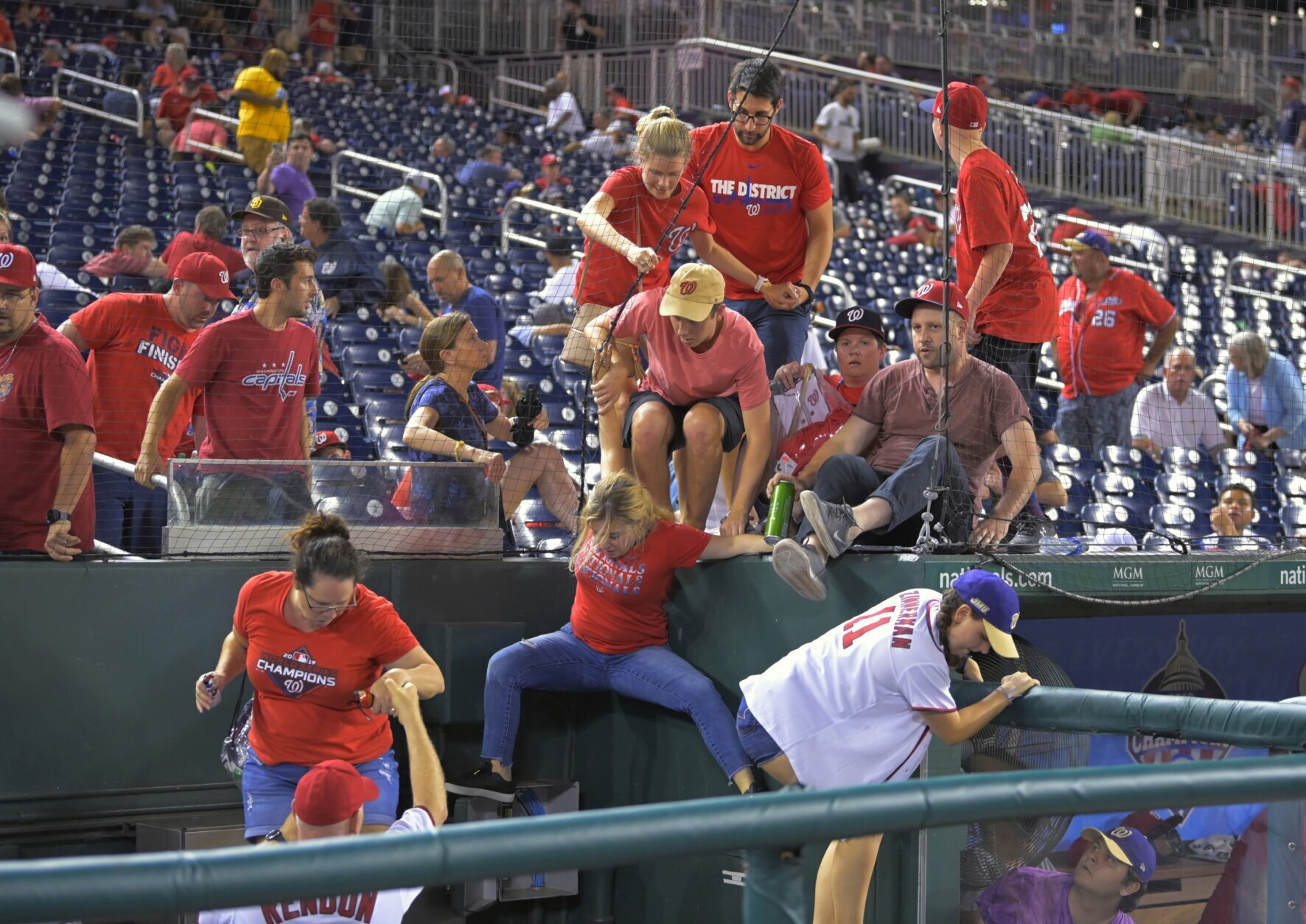 Fans jump into a camera well after hearing gunfire from outside the stadium, during a baseball game between the San Diego Padres and the Washington Nationals at Nationals Park in Washington on Saturday, July 17, 2021. (John McDonnell/The Washington Post via AP)