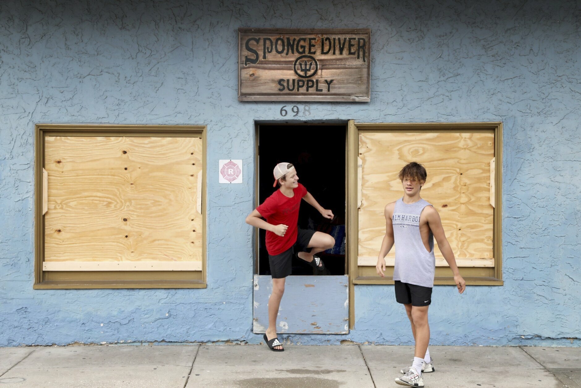 Athos Karistinos, 13, center, and his brother, Anastasios Karistinos, 16, emerge from their family's gift shop, Sponge Diver Supply, after helping their father fortify the windows and doors at the business on Dodecanese Blvd at the Tarpon Springs, Fla., Sponge Docks on Tuesday, July 6, 2021, where residents and business owners were preparing for the arrival of Tropical Storm Elsa. (Douglas R. Clifford/Tampa Bay Times via AP)