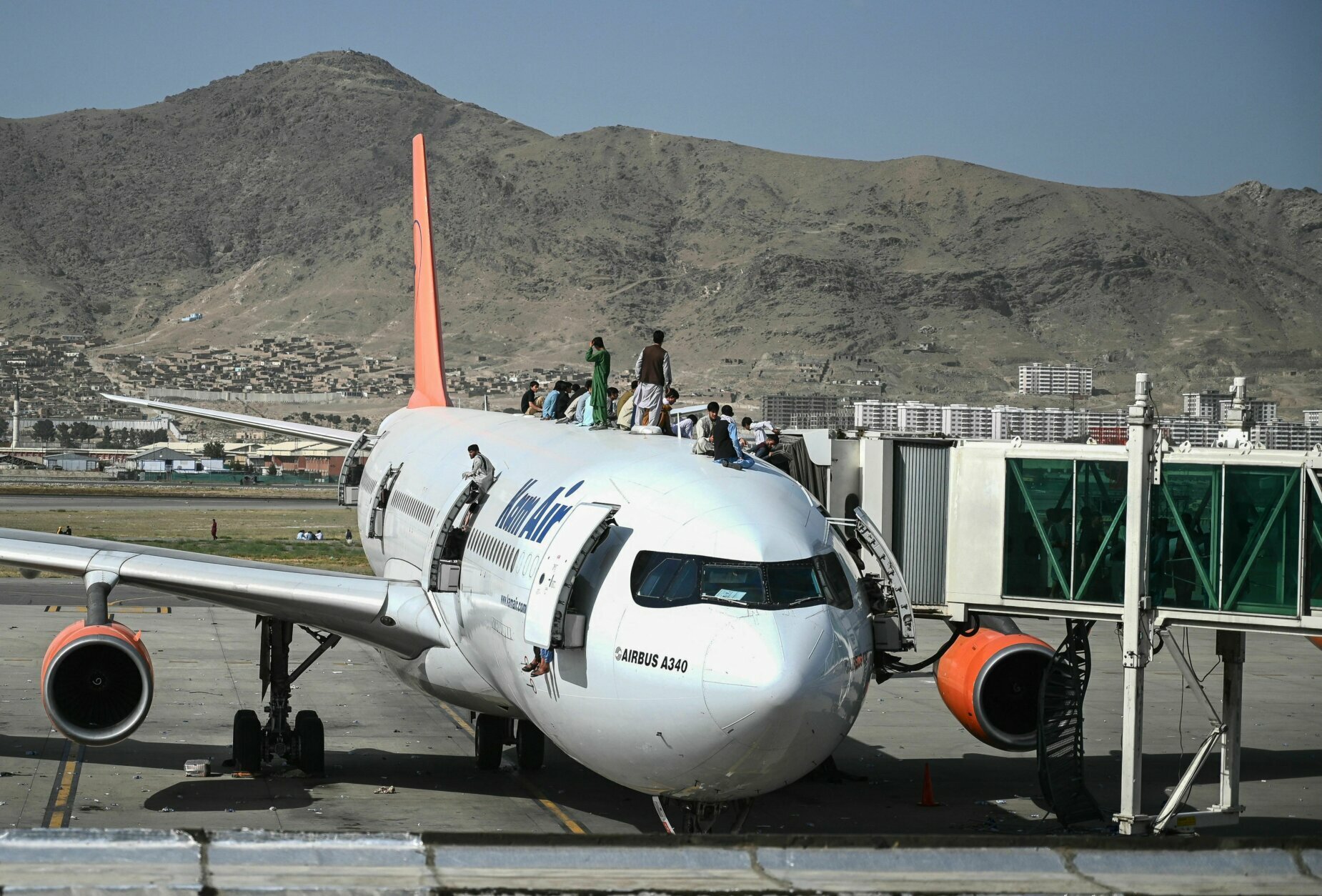 Afghan people climb atop a plane as they wait at the Kabul airport in Kabul on August 16, 2021, after a stunningly swift end to Afghanistan's 20-year war, as thousands of people mobbed the city's airport trying to flee the group's feared hardline brand of Islamist rule. (Photo by Wakil Kohsar / AFP) (Photo by WAKIL KOHSAR/AFP via Getty Images)