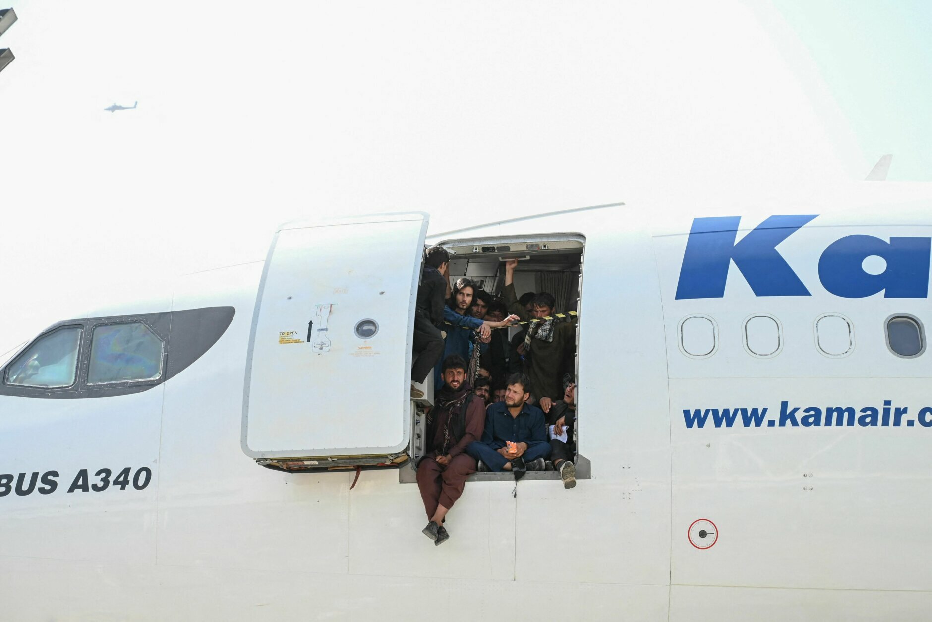TOPSHOT - Afghan people climb up on a plane and sit by the door as they wait at the Kabul airport in Kabul on August 16, 2021, after a stunningly swift end to Afghanistan's 20-year war, as thousands of people mobbed the city's airport trying to flee the group's feared hardline brand of Islamist rule. (Photo by Wakil Kohsar / AFP) (Photo by WAKIL KOHSAR/AFP via Getty Images)
