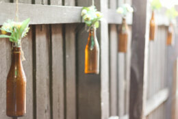 <p><strong>Reuse bottles as hanging vases along the fence.</strong> Empty glass bottles are used in a variety of ways in the garden and make a great hanging vase. Use many or just a few for a simple addition of temporary flowers.</p>
