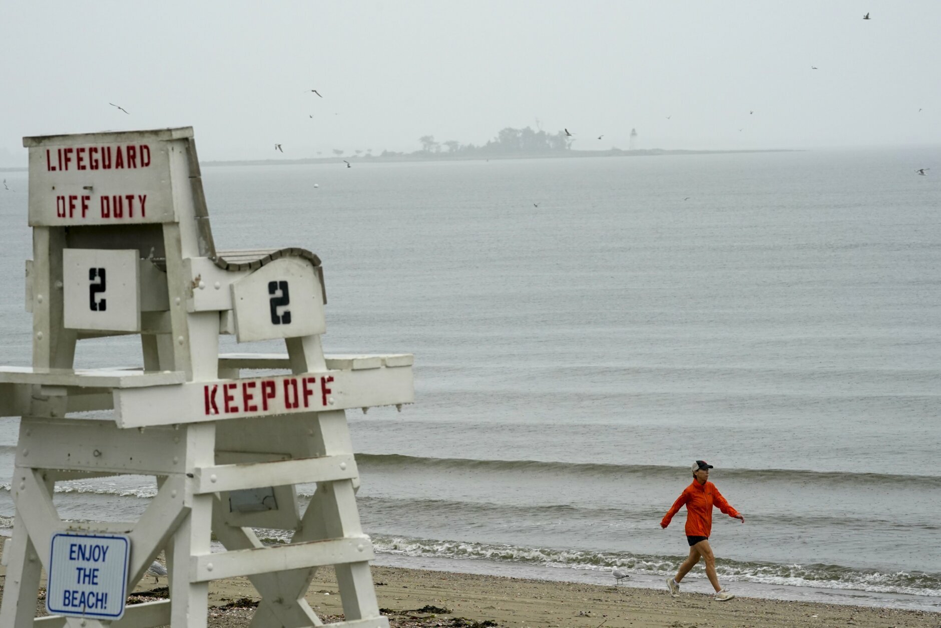 A woman walks in the rain fall on Penfield beach as Tropical Storm Henri approaches, Sunday, Aug. 22, 2021, in Fairfield, Conn. (AP Photo/Mary Altaffer)