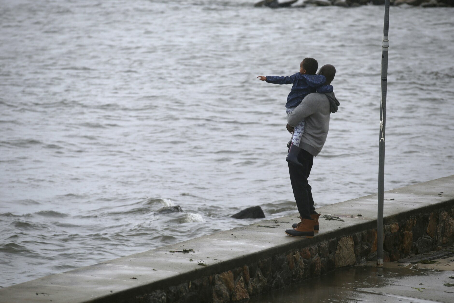 David Jeancy, from New London, Conn., holds his son Grant as they watch the waves from Pequot Point beach as Tropical Storm Henri approaches, Sunday, Aug. 22, 2021, in New London, Conn. (AP Photo/Stew Milne)