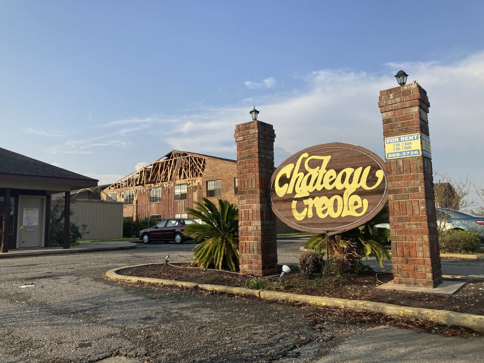 Behind a sign for the Chateau Creole apartment complex, Sunday, Sept. 5, 2021, can be seen damage from Hurricane Ida. The storm caused such extensive damage to the buildings in the complex that residents have to move out. (AP Photo/Rebecca Santana)