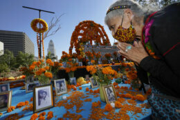 Ofelia Esparza, 88, from East Los Angles, has brough fresh marigolds, often called "flowers of the dead," and placed them next to pictures of family members who died in 2020, at an altar for Day of the Dead, titled "2020 Memorial to Our Resilience," at Grand Park in Los Angeles, Thursday, Oct. 29, 2020. Day of the Dead, or Dia de los Muertos, the annual Mexican tradition of reminiscing about departed loved ones with colorful altars, or ofrendas, is typically celebrated Sunday through Monday. It will undoubtedly be harder for Latino families in the U.S. torn apart by the coronavirus. (AP Photo/Damian Dovarganes)
