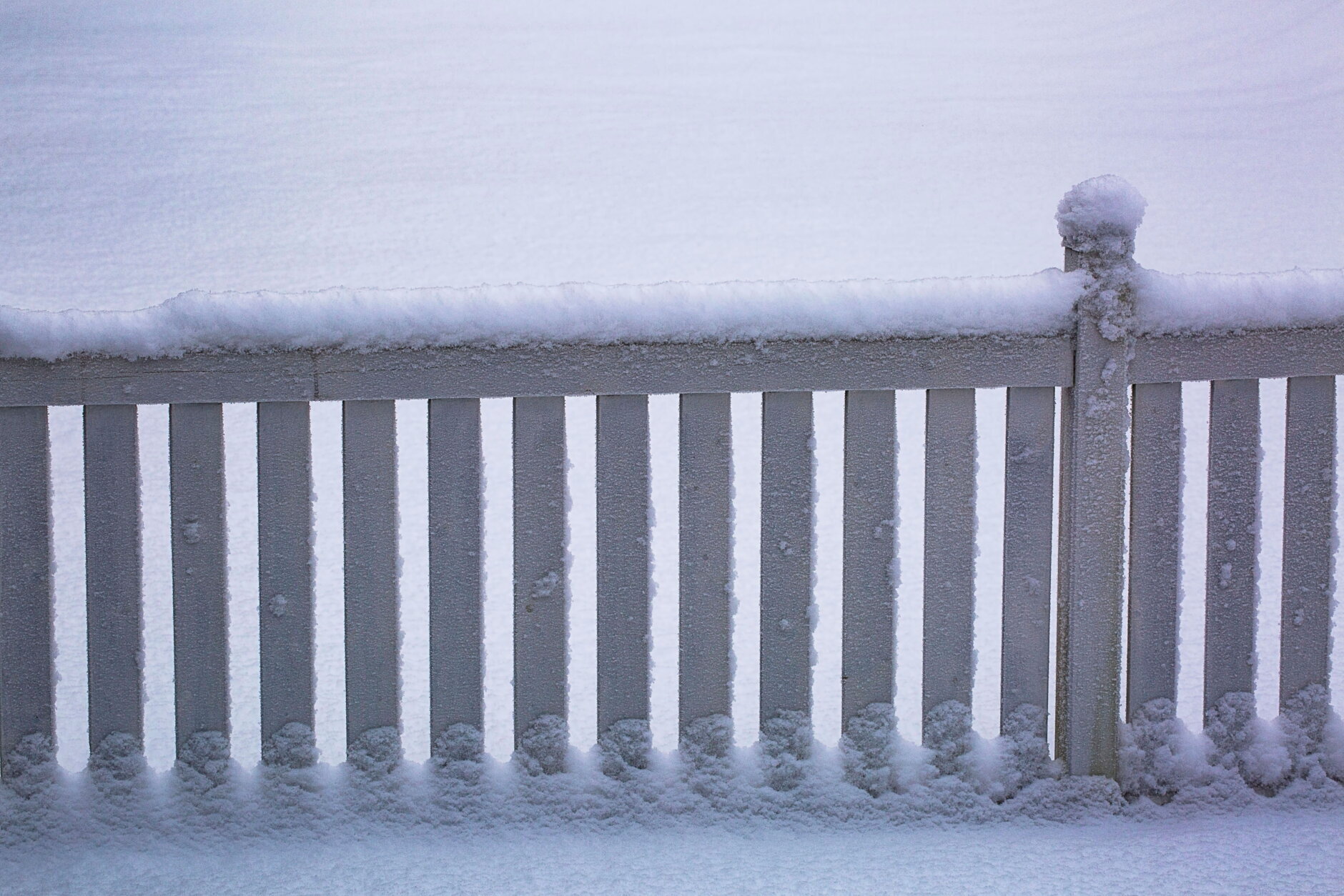 Beautiful snow winter background. White wooden fence covered with snow.