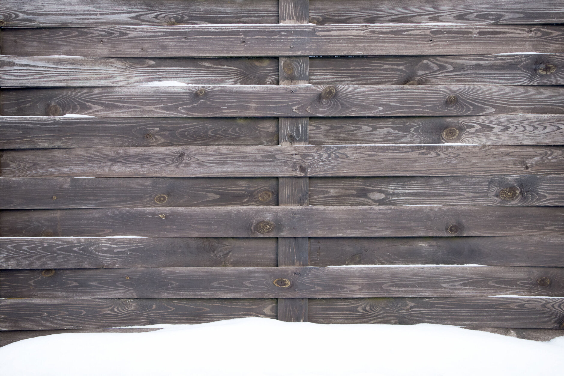 Old snowed wooden fence of grey unplanned planks, may be used as background or texture