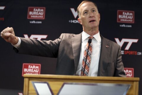 man speaks at podium pointing right arm to the side