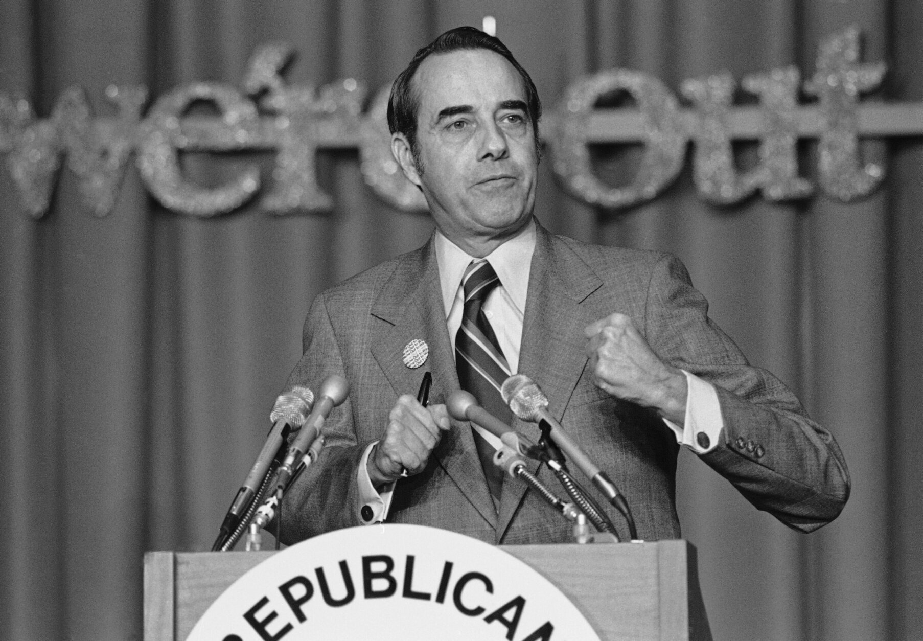 Sen. Robert Dole of Kansas, a former GOP national chairman, addresses the Republican Leadership Conference in Washington Friday, March 7, 1975. Dole said, "at least in terms of numbers the Republican Party is today in worse shape than it has ever been before in its history." The full sign behind him reads "we're out to win". (AP Photo)