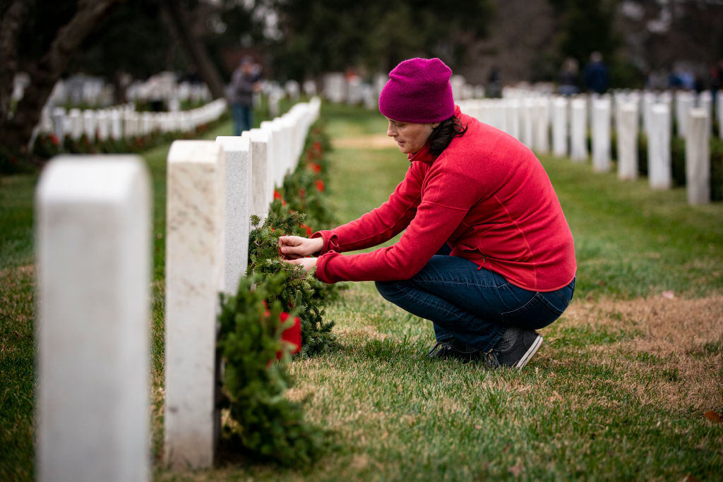 ARLINGTON, VA - DECEMBER 18: A woman places a wreath on a tombstone at Arlington National Cemetery, on December 18, 2021 in Arlington, Virginia. The 30th annual Wreaths Across America project places wreaths on the more than 250,000 tombstones of military servicemen and women at Arlington National Cemetery. (Photo by Al Drago/Getty Images)