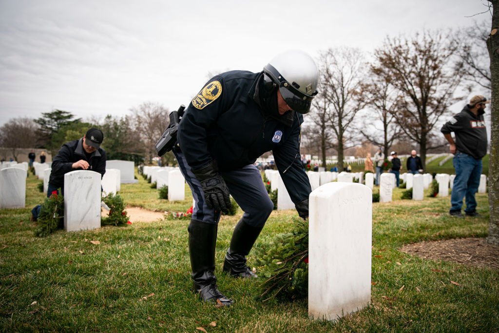 ARLINGTON, VA - DECEMBER 18: A Virginia State Police officer places a balsam fir wreath on a tombstone, at Section 60 at Arlington National Cemetery, on December 18, 2021 in Arlington, Virginia. The 30th annual Wreaths Across America project places wreaths on the more than 250,000 tombstones of military servicemen and women at Arlington National Cemetery. (Photo by Al Drago/Getty Images)
