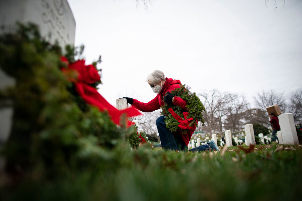 A woman places a wreath on a tombstone at Arlington National Cemetery, on December 18, 2021 in Arlington, Virginia. (Getty Images/Al Drago)