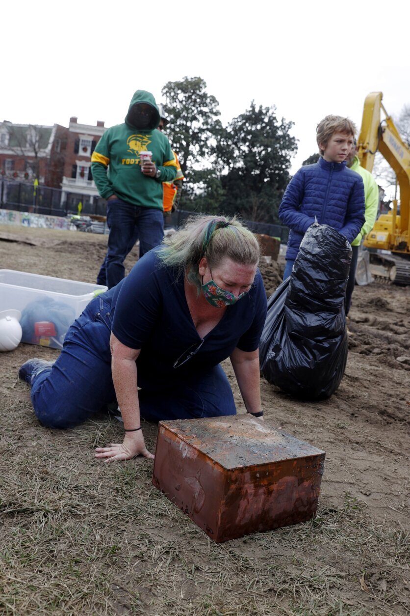 Katherine Ridgway, state archaeological conservator, prepares to wrap and remove a box believed to be the 1887 time capsule that was put under Confederate Gen. Robert E. Lee statue's pedestal Monday, Dec. 27, 2021, in Richmond, Va. In back, Everett Mercer, 10, son of Governor Ralph Northam's chief staff Clark Mercer, stands by to help. Crews wrapping up the removal Monday of the giant pedestal that once held a statue of Gen. Lee found what appeared to be a second and long-sought-after time capsule, Virginia Gov. Ralph Northam said.  (Eva Russo/Richmond Times-Dispatch via AP)