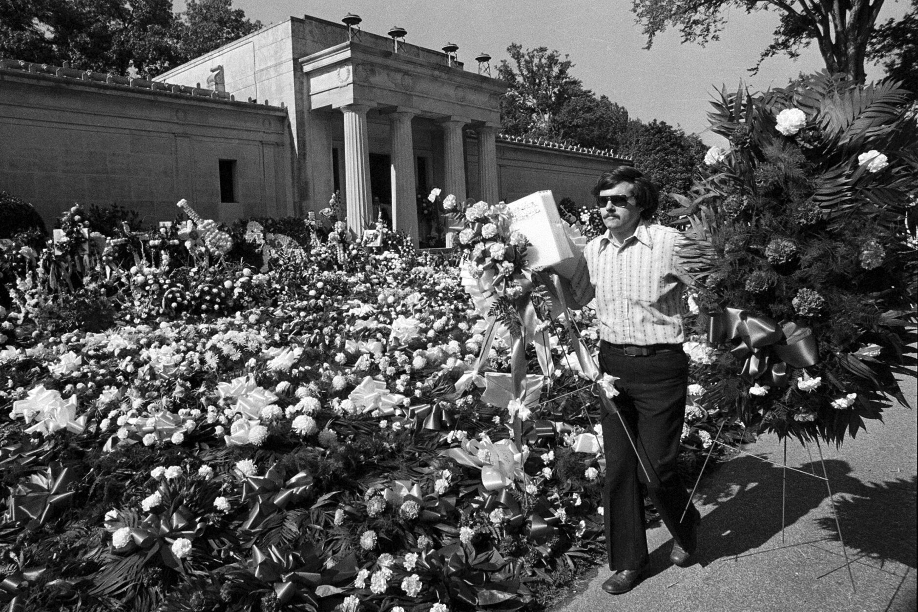 FILE - A florist adds more floral arrangements to the overflowing collection of flowers that cover the ground at the mausoleum Aug. 18, 1977, where singer Elvis Presley was entombed during funeral services in Memphis, Tenn. (AP Photo, File)