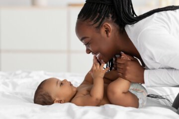 African American mom playing in bed with her baby